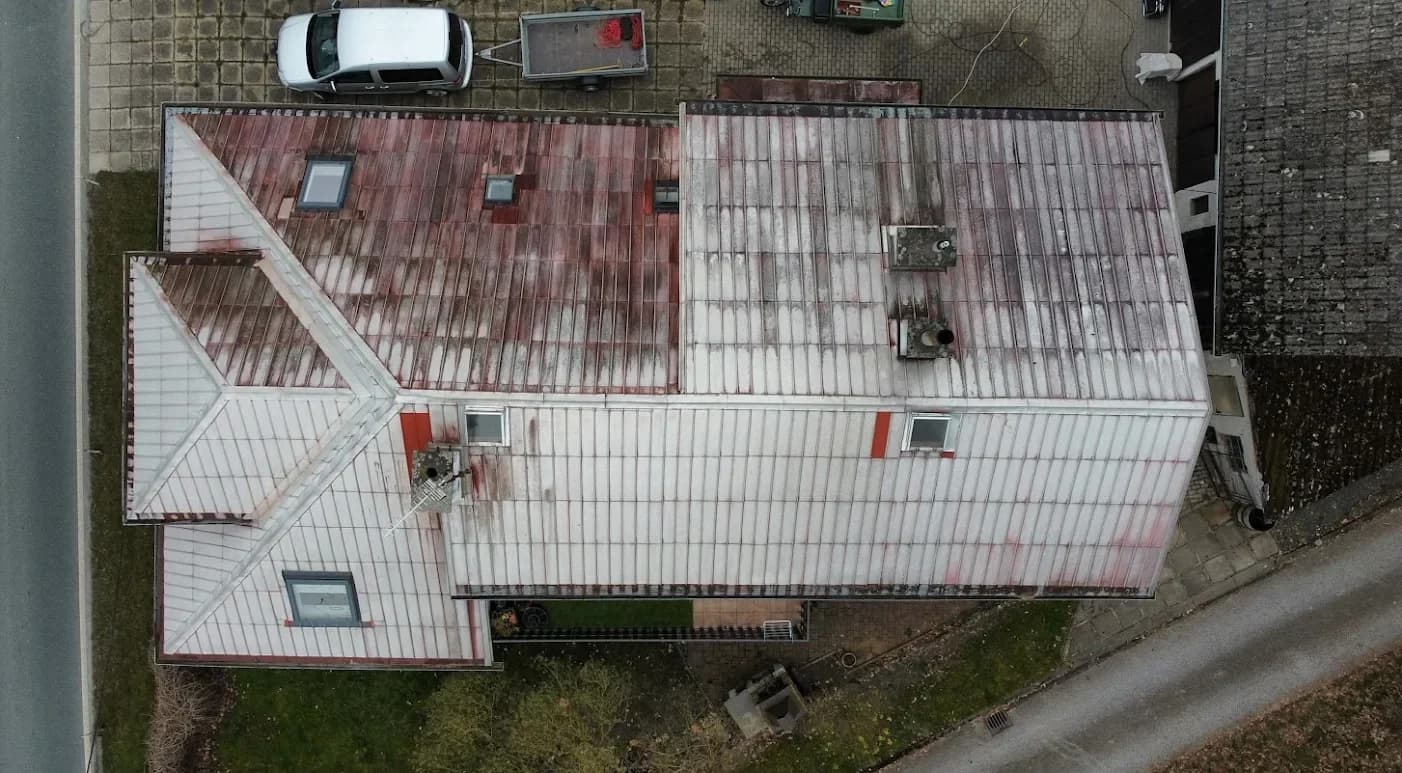 Plechová střecha rodinného domu před renovací, vybledlý a zoxidovaný nátěr s bílými mapami.