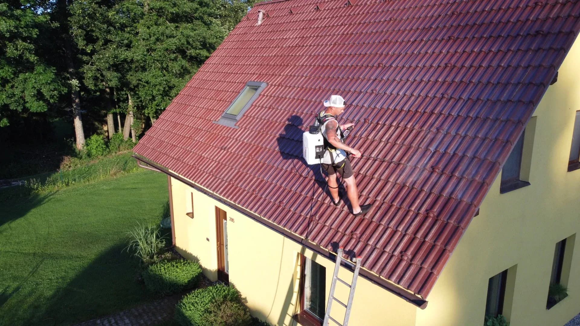 Pracovník RabatClean nanáší ochranný nátěr na červenou taškovou střechu, letecký pohled.