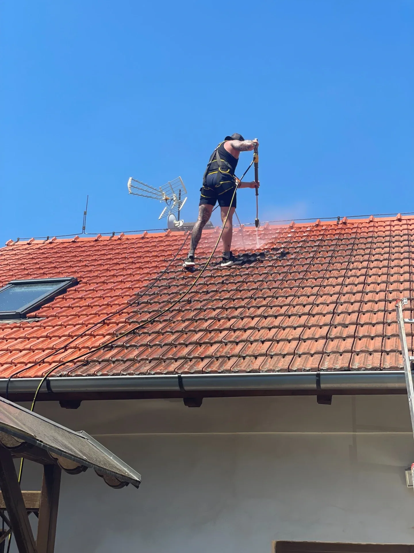 Vysokotlaké čištění taškové střechy, pracovník v jisticím postroji s tryskou.